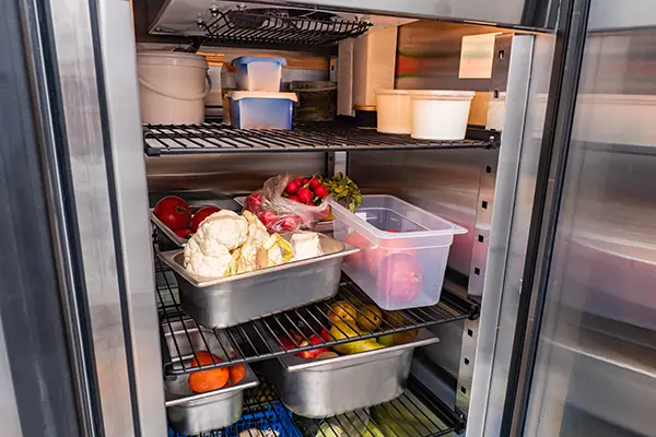 Refrigerator of restaurant with food. Vegetables in restaurant refrigerator. Containers with vegetables on shelves of refrigerator. Radishes, cauliflower and pears in fridge containers